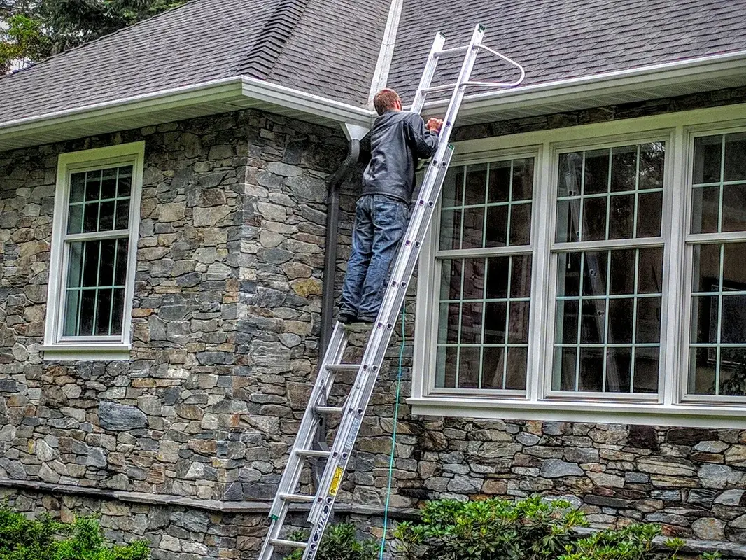 A ladder set against a stone-clad house at the roof edge